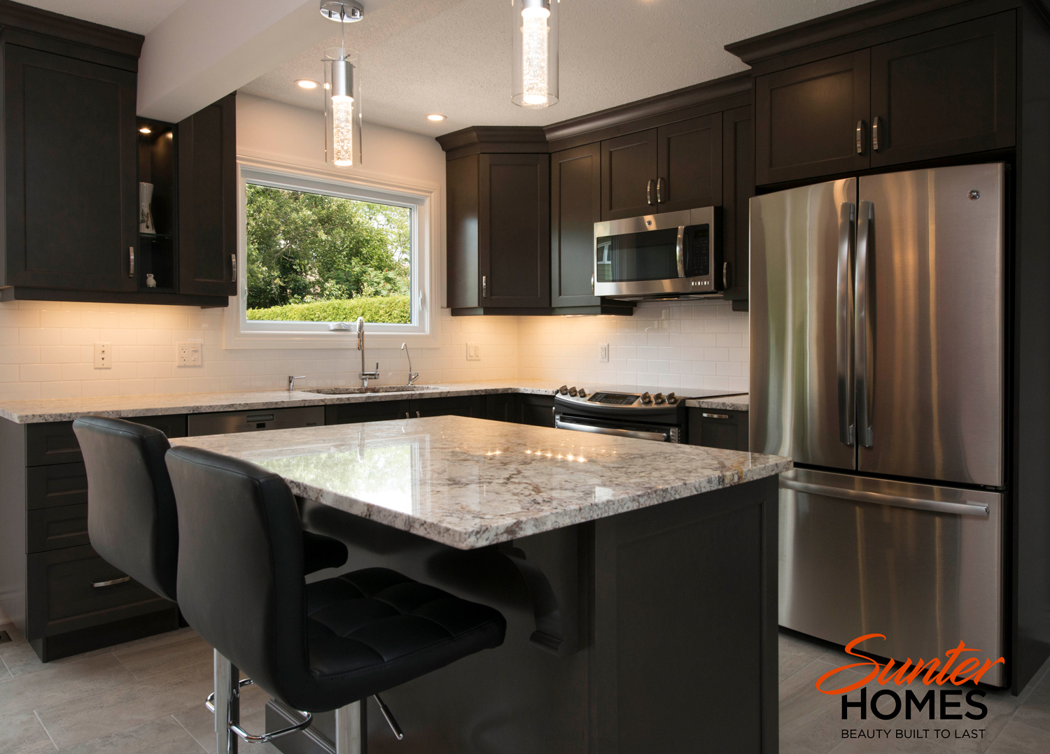 A beautifully renovated contemporary kitchen in the Ottawa area, with modern light features and an island with two chairs for light meals.