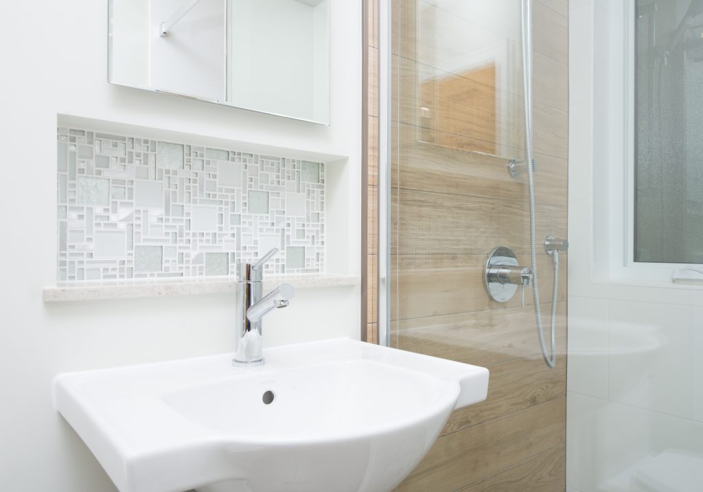 A beautiful view of an inset shelf behind a sink, next to a glass-enclosed shower with beautiful tile features.
