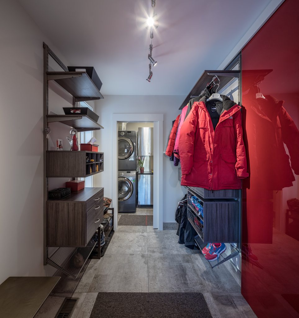 A modern, stylish mudroom with red a red wall and a red jacket hanging up offers a look into the home beyond.