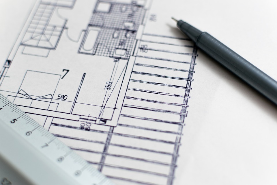 A set of floorplans sits on a table, with a pen and ruler resting on top.