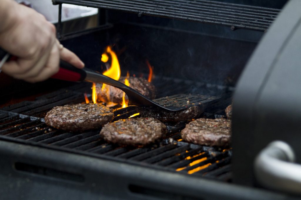 A person flips burgers on a barbecue grill.