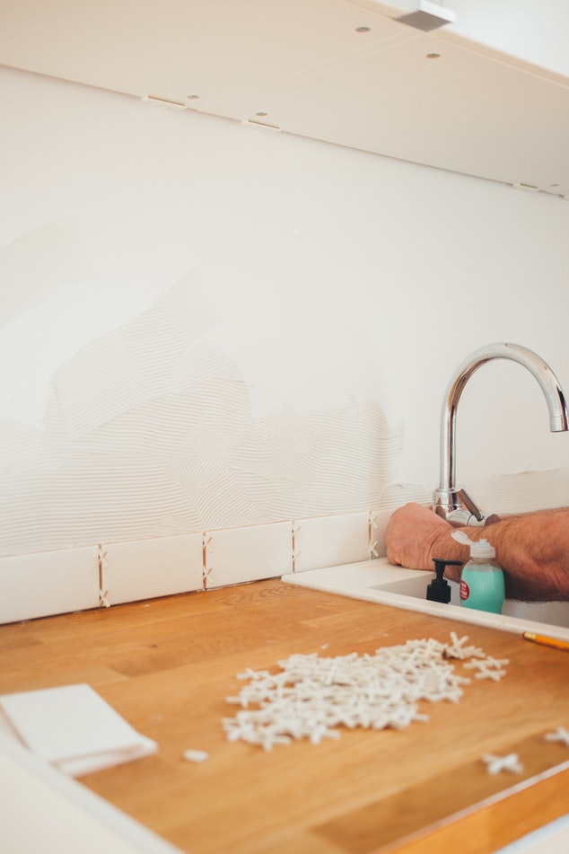 A contractor sets kitchen tile behind a sink and countertop to create a backsplash.