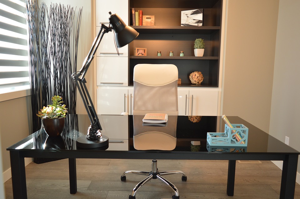 A simple, modern desk set up with a lamp sits in front of a large shelving unit with built-in cupboards and drawers.