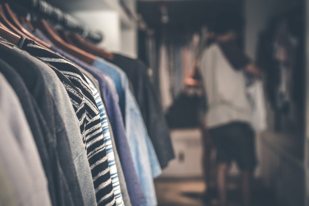 Shirts hang on the rack in a walk-in closet as a man looks for clothes in front of a mirror.